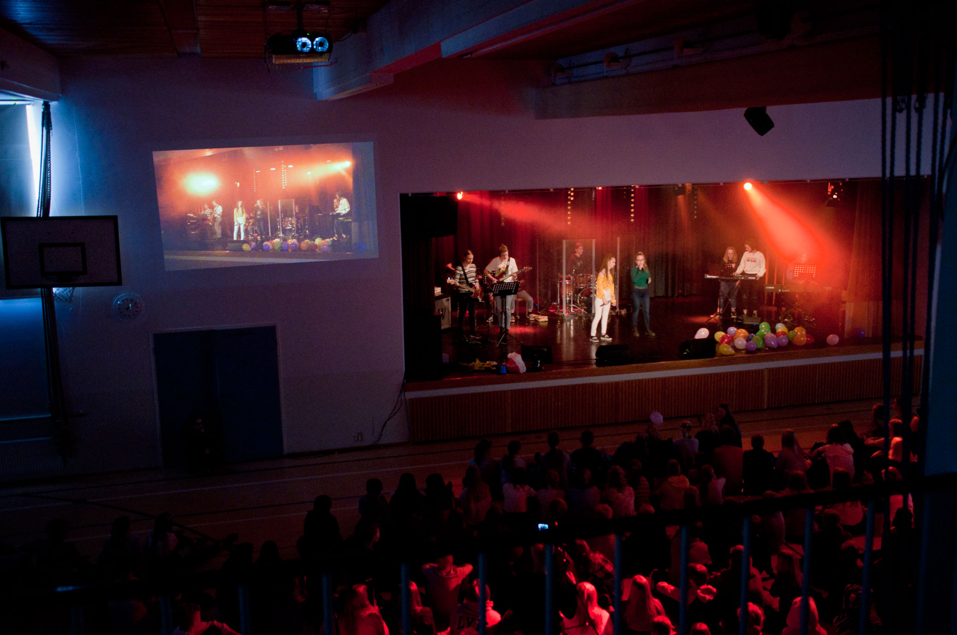 Vappukonsertti. Juhlasalin lava on valaistu punaisilla valoilla ja lavalla on soittajia. 