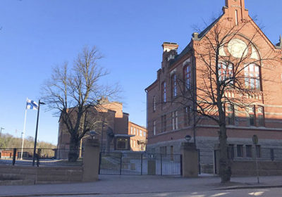 Suomen lippu liehuu tuulessa Lahden yhteiskoulun vanhan koulurakennuksen vierellä aurinkoisena talvipäivänä.