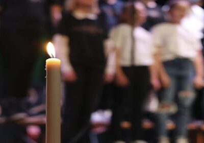 1. adventtia kuvaava kynttilä, taustalla sumennettuna musiikkiluokkien kuorolaisia.