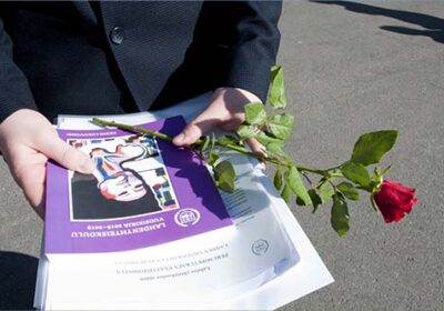 Oppilas tummassa puvussa. Kädessä punainen ruusu, Lahden yhteiskoulun vuosikirja ja 9. luokan päättötodistus.