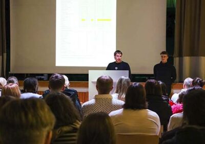 Peruskoulun vanhempainilta. Kaksi opettajaa puhumassa oppilaiden vanhemmille juhlasalissa.