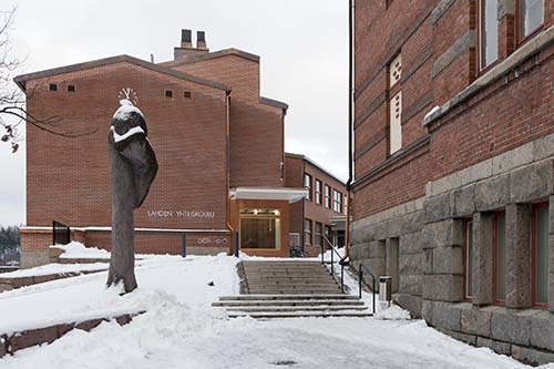 Lahden yhteiskoulun punatiiliset koulurakennukset Siipi ja Museo talvella. Rakennusten välissä on Olavi Lanun Yhteispuu-veistos, jossa on kaksi halaavaa ihmishahmoa.