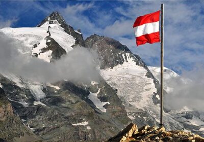 Itävallan lippu liehuu vuoriston huipulla. Taustalla luminen vuorenhuippu.
