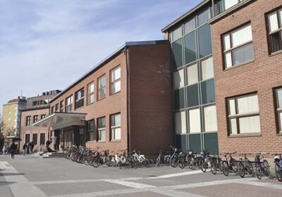 Punatiilinen koulurakennus ja koulun piha. Pihalla oppilaita ja polkupyöriä.
