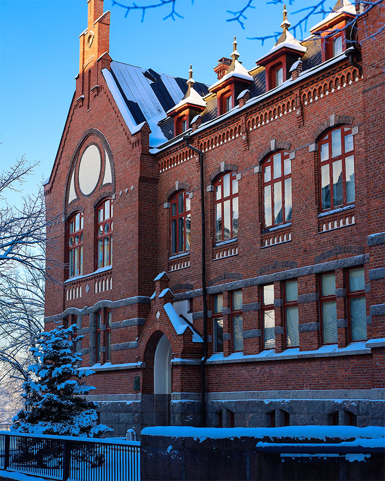 Lahden yhteiskoulun historiallinen punatiilinen koulurakennus talvimaisemassa Kirkkokadulla, lumipeitteiset katot ja kirkas sininen taivas.