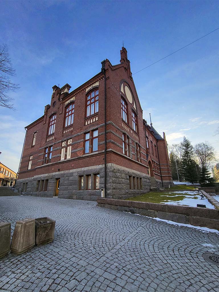 Lahden yhteiskoulun vanha koulurakennus aurinkoisena kevätpäivänä kuvattuna. Maassa on vielä hiukan lunta ja aurinko paistaa siniseltä taivaalta rakennuksen takaa.