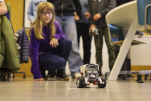 Etualalla kyykyssä oleva oppilas seuraa robottia luokassa osana LUMA‑opetusta, taustalla on muita oppilaita.