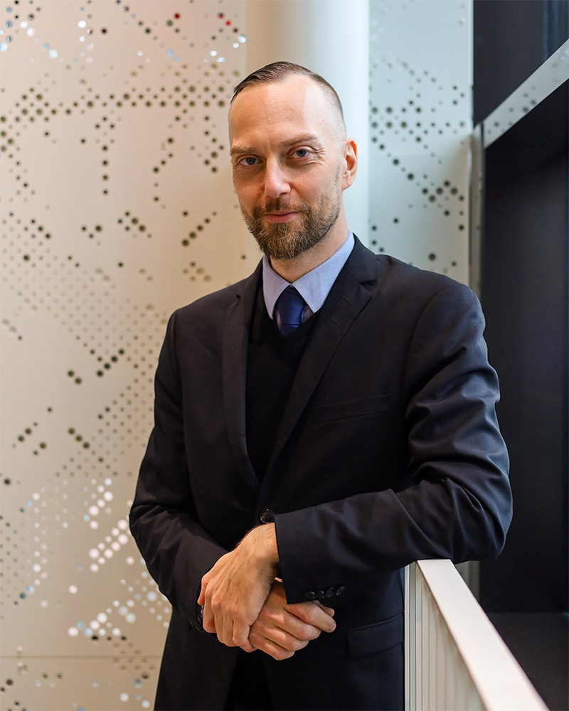 Vuoden lykkiläinen 2025 Ilmari Kaihkö nojaa hymyillen kaiteeseen valoisassa porraskäytävässä.