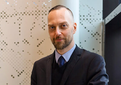 Vuoden lykkiläinen 2025 Ilmari Kaihkö nojaa hymyillen kaiteeseen valoisassa porraskäytävässä.