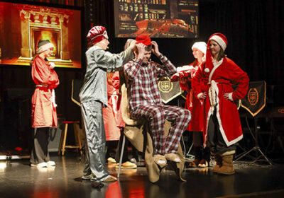 Joulujuhlanäytelmä koulun lavalla. Nuoria pyjamissa, tonttulakeissa ja yksi pukeutuneena joulupukiksi.